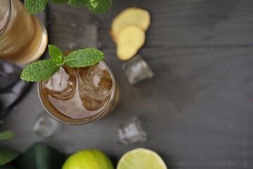 Glass of tasty ginger ale with ice cubes and mint on grey wooden table, top view. Space for text