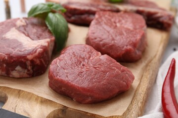 Cut fresh beef meat with basil leaves on wooden board, closeup