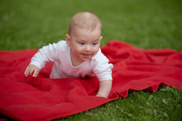 Sweet dream on a red blanket. A little kid is lying on the soft grass, on a bright blanket. His cute face and hands look so calm and happy.