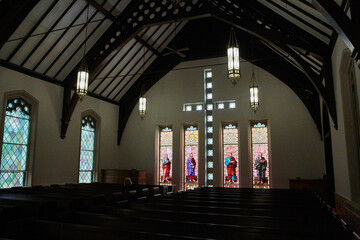 Church pews, hanging chandeliers, demon, creepy, stained glass religious windows depicting saints - obrazy, fototapety, plakaty