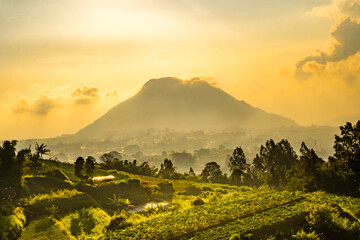 View of Merbabu Mountain in Indonesia during hazy sunset with green village foreground.