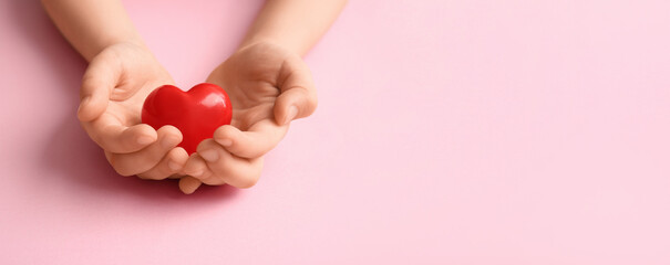 Child's hands with red heart on pink background with space for text