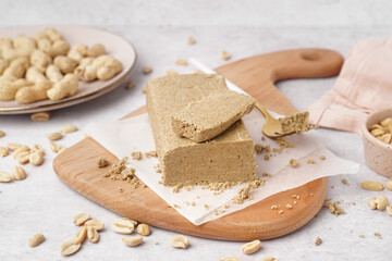 Board with tasty halva and peanuts on white background