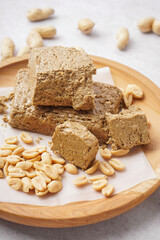 Wooden plate with pieces of tasty halva and peanuts on white background