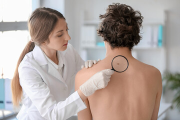 Dermatologist examining mole on young man's back with magnifier in clinic