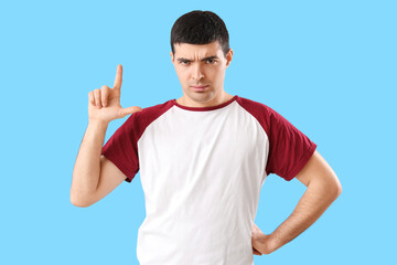 Upset young man showing loser gesture on blue background