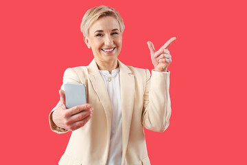 Happy mature woman with phone pointing at something on red background