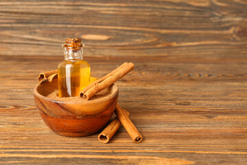 Obraz na płótnie Canvas Bowl with bottle of essential oil, cinnamon powder and sticks on wooden background