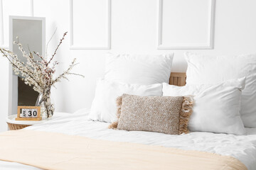 Bed with many pillows and blooming tree branches on bedside table