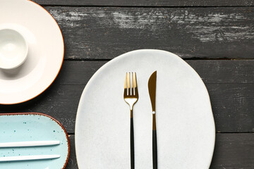 Table setting with clean plates and cutlery on black wooden table