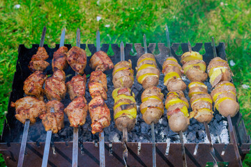 Portable metal brazier is used to grill kebab skewers and potatoes with bacon on skewer