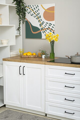 Interior of stylish kitchen with blooming narcissus flowers in vase on counter