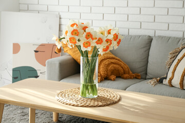 Fototapeta na wymiar Vase with blooming narcissus flowers on table in light living room