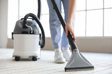 Fototapeta premium Young woman hoovering carpet at home, closeup