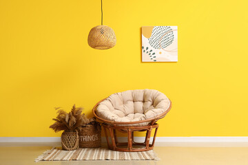 Cozy armchair and vase with pampas grass near yellow wall