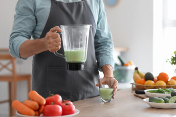 Mature man pouring fresh smoothie from blender into glass in kitchen, closeup