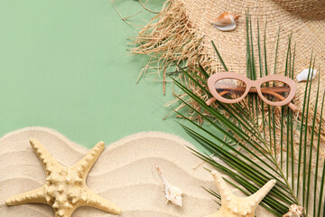 Composition with palm leaf, sand, seashells and beach accessories on green background