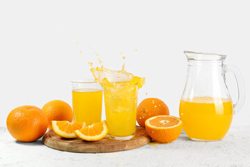 Jug and glasses of fresh orange juice with splashes on white background