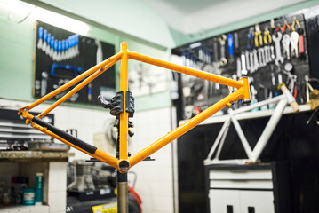Orange bicycle frame held on a stand in a mechanical bike repair shop. Composition with copy space without people.