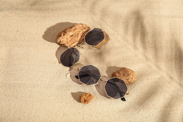 Fototapeta na wymiar Stones with stylish sunglasses on sand