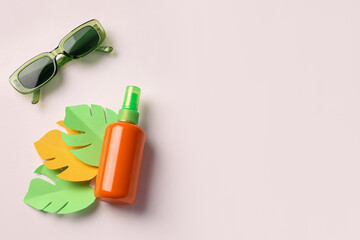 Bottle of sunscreen cream with paper palm leaves and sunglasses on white background