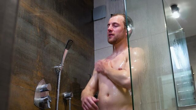 Handsome naked man taking shower in hotel bathroom