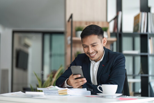 Happy young Asian business man with a smile using smartphone at the office