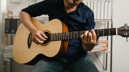 Obraz premium Young joyful asian handsome man playing guitar at home.