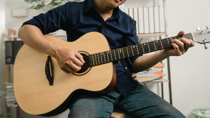 Obraz premium Young joyful asian handsome man playing guitar at home.