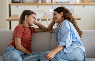 Loving mother listening to daughter with empathy and understanding while sitting together on sofa bonding at home, pre-teen girl child sharing secrets with mom, parent communicating with teenager - obrazy, fototapety, plakaty