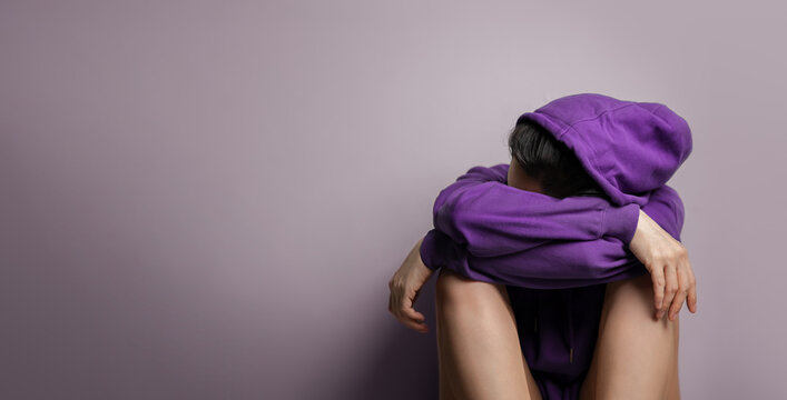 Mental Health Concept. a Stress, Anxiety, Depression Hoodie Women sitting by the Wall. more copy space on the left. Purple Blue Tone
