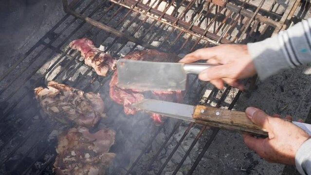 hands view senior man cutting and grilling meat on outdoor grill