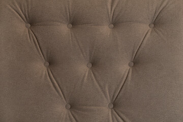 Upholstery in beige fabric with a structured pattern on buttons for an interior close-up. Quilted vintage brown fabric sofa background. Carriage coupler for furniture.