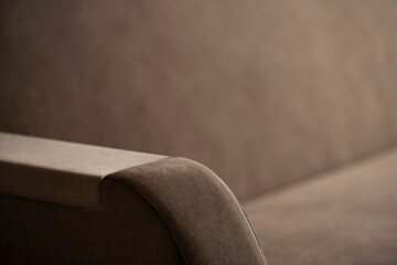 The side of the sofa in a fleecy beige fabric close-up with a blurry place for text. An element of upholstered furniture for hands in two-tone fabric covering in shadows and highlights.