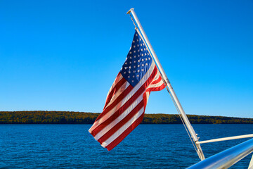 American flag hanging off boat with distant shore and calm lake or river waters