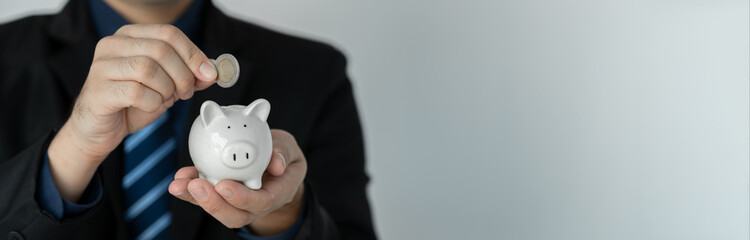 copy-space, banner, panorama Businessman holding a piggy bank and putting coins into the piggy bank The concept of saving money, investing, financial planning.