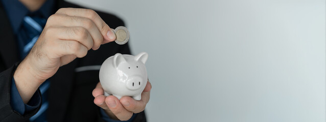 copy-space, banner, panorama Businessman holding a piggy bank and putting coins into the piggy bank...