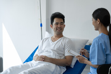 Physiotherapist giving advice and encouragement to male patient doing physiotherapy lying on...
