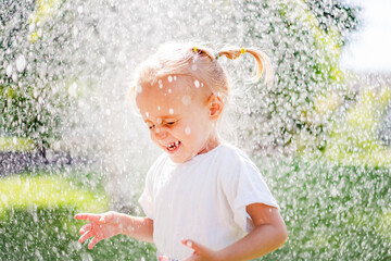 A beautiful girl in a dress plays on a green lawn and splashes with water