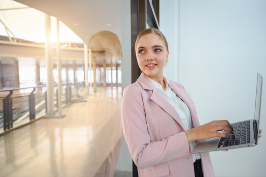 A successful business woman female employee of a company smiling and holding laptop standing by the mirror in the office
