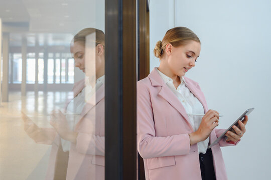 Portrait of a young business woman Confident standing and smiling company worker looking at digital tablet and holding digital tablet beside glass in office