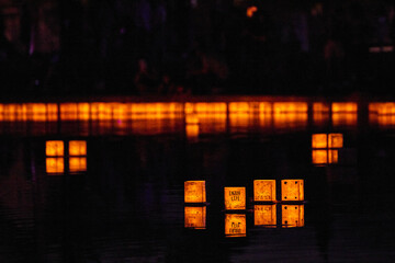 Golden glowing wall of lanterns in background as four float quietly on pond