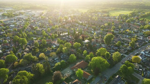 Aerial of a beautiful green suburban neighborhood at golden hour. The sun shines a flare in the camera
