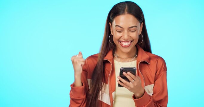 Woman with smartphone, fist pump and celebration with happiness, bonus and winning on blue background. Mockup space, tech and online competition, happy female person with reward and win in studio