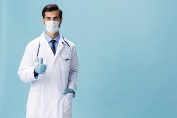 Male doctor in a white coat and medical mask shows hand gestures and looks at the camera on a blue isolated background, copy space, space for text