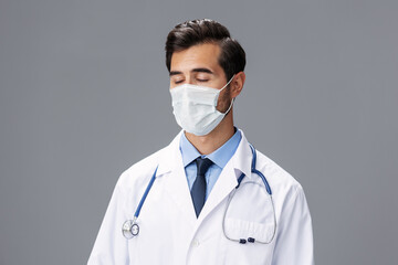 A male doctor in a white coat and medical mask and sterile gloves looks at the camera on a gray isolated background, copy space, space for text