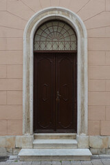 Fototapeta na wymiar street view of old wooden door with arched frame against pink wall in Croatia