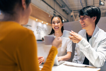 Group of Asian friends talking and using laptop computer in restaurant. 