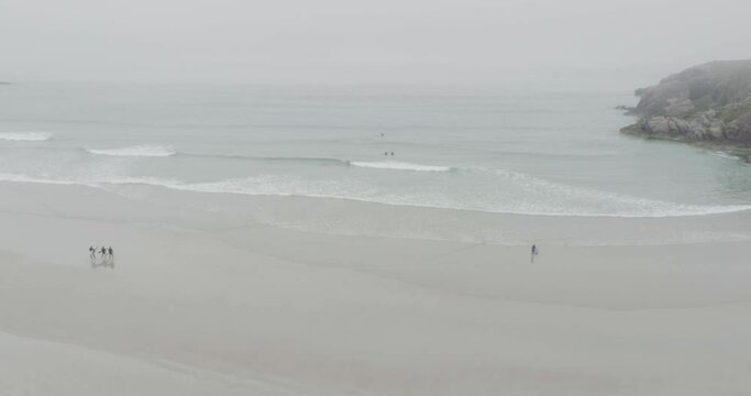Surfers and big waves on Ceannabeinne Beach on the Scotland North Coast 500 Route which is the North Sea