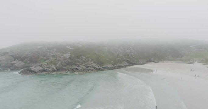 Drone shot of surfers, big waves and misty weather on Ceannabeinne Beach on the Scotland North Coast 500 Route which is the North Sea